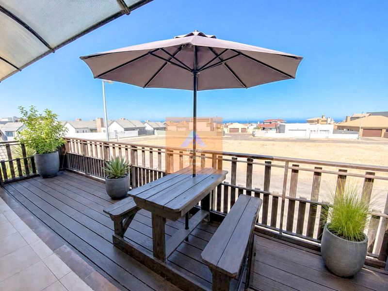 An elevated timber balcony featuring a protective roof covering and wooden balustrades, offering an open outdoor space with neighbourhood and distant sea views.