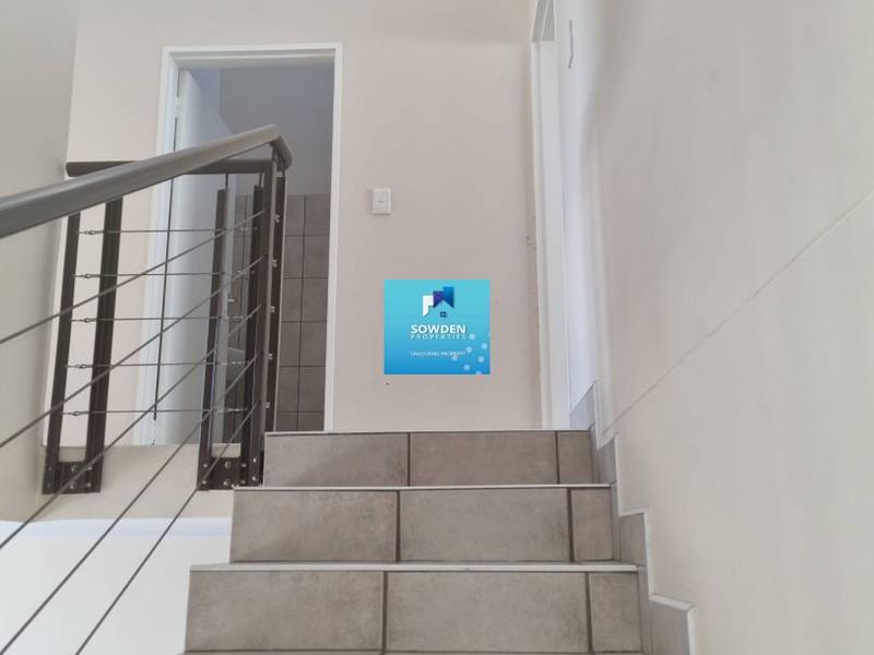 A bright, double-volume hallway featuring a tiled staircase with a modern metal balustrade, leading to an upper level.