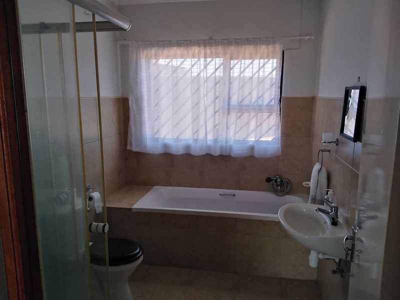 A functional bathroom featuring a built-in bathtub, separate shower enclosure, wall-mounted basin, and toilet with neutral wall tiling.