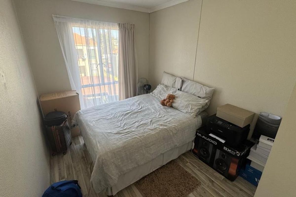 A compact bedroom featuring laminate flooring and a large window with curtain tracks, providing natural light to the space.