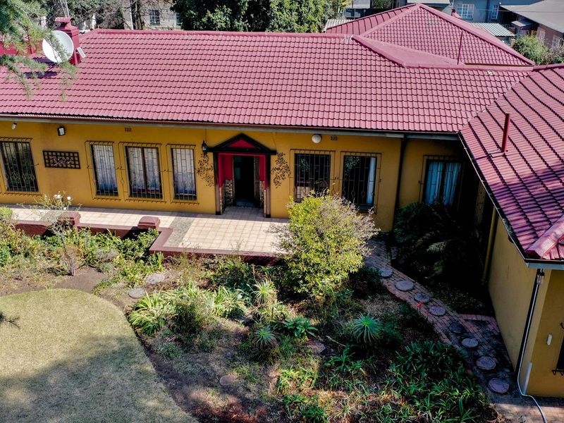 Aerial view of a single-story house featuring a tiled roof, paved patio area, and established garden with security bars on windows.