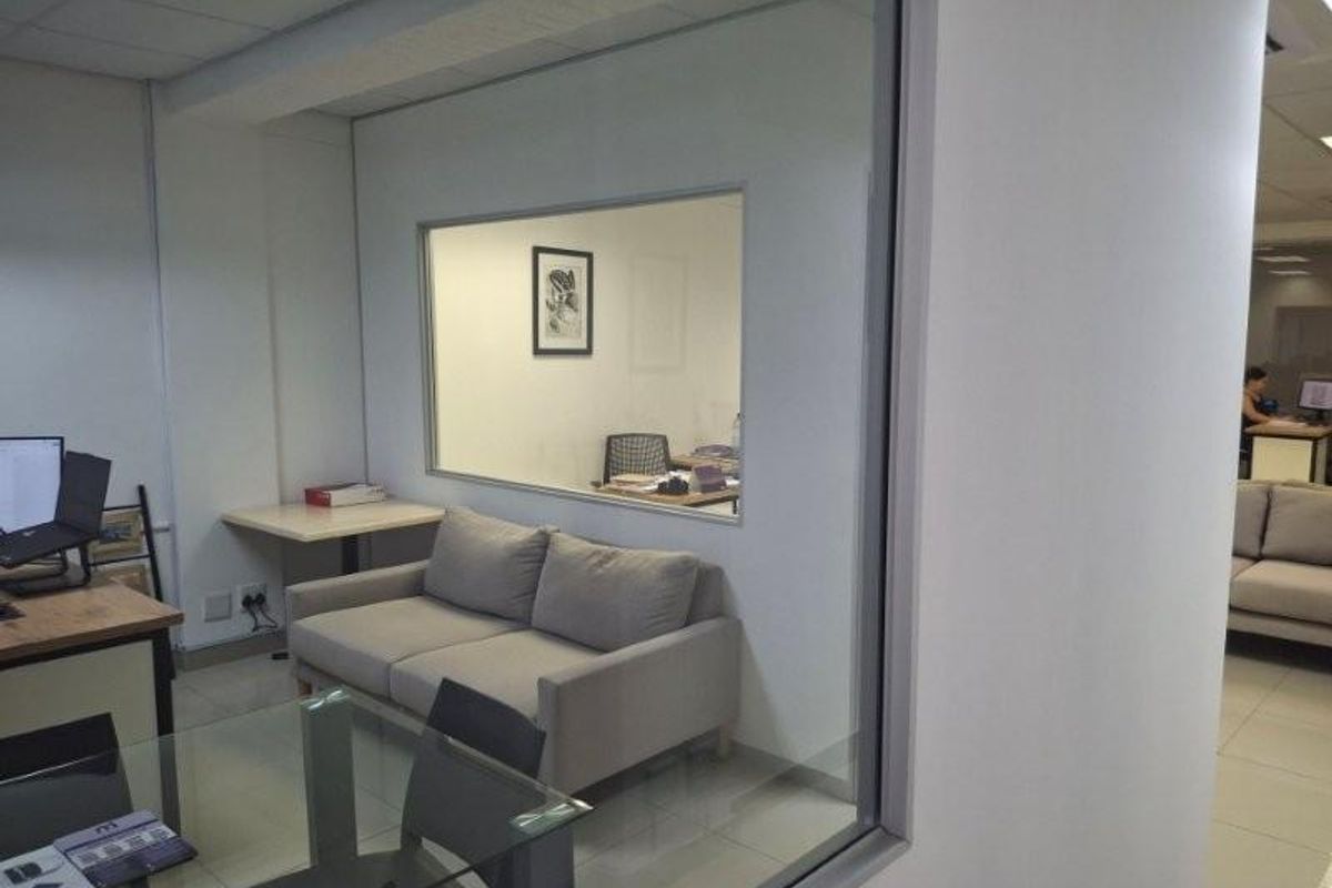 A professional office space featuring a glass partition wall, suspended ceiling with recessed lighting, and neutral tiled flooring.