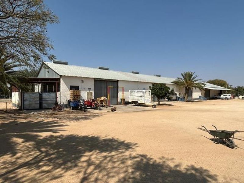 A wide-angle view of an industrial warehouse facility featuring a large corrugated metal roof, sliding access doors, and a spacious gravel yard area.