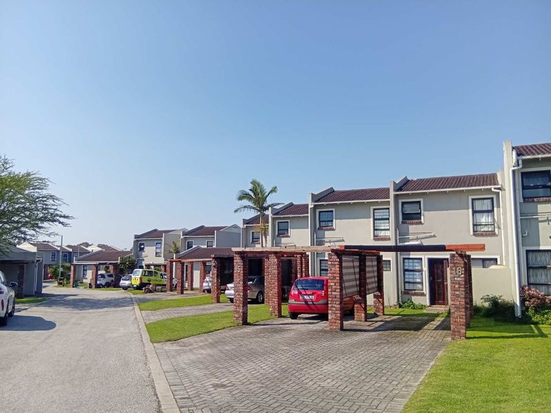 Street view of a townhouse complex featuring brick-paved driveways, timber-framed carports, and tiled roof facades.