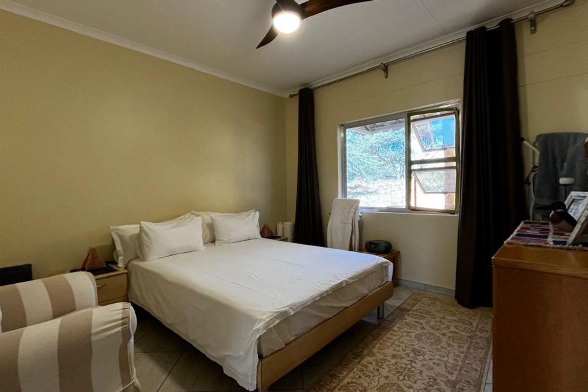 A comfortable bedroom featuring tiled flooring, a ceiling fan, and a window providing natural light.