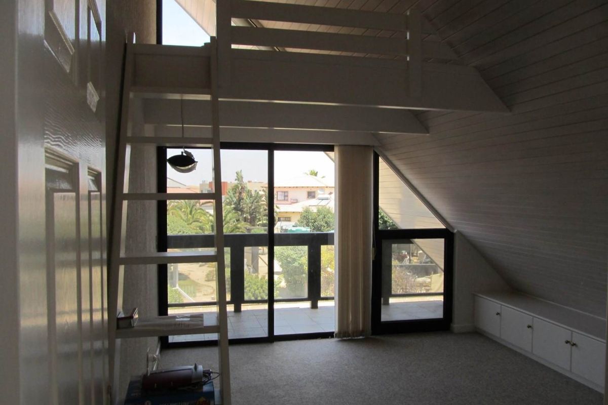 Spacious bedroom featuring a loft area, built-in storage, sloped timber ceilings, and direct access to a private balcony through sliding glass doors.