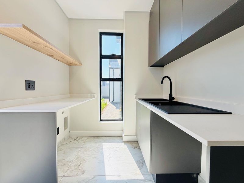Modern scullery featuring sleek grey cabinetry, white stone countertops, a black sink with matching tapware, and tiled flooring.
