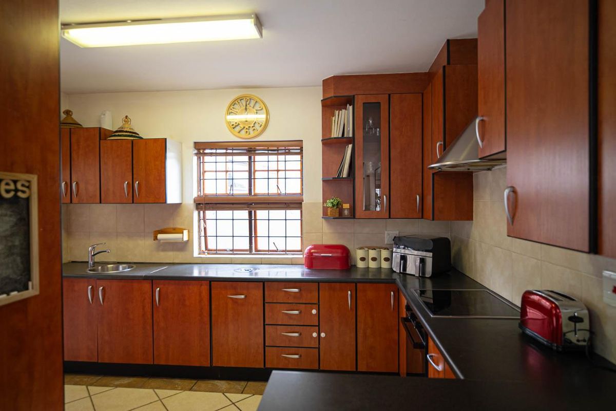 A functional kitchen featuring wood-finish cabinetry, dark countertops, a built-in hob, and an extractor fan, with tiled flooring and a window providing natural light.
