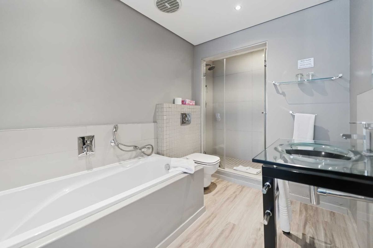 Modern bathroom featuring a built-in bathtub, glass-enclosed shower, wall-mounted toilet, and a contemporary glass vanity basin with wood-look flooring.