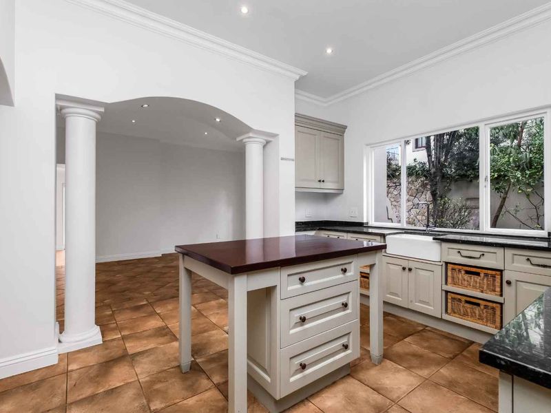 A bright, well-maintained kitchen featuring a central island, granite countertops, a farmhouse sink, and elegant architectural archways leading to an adjacent living space.