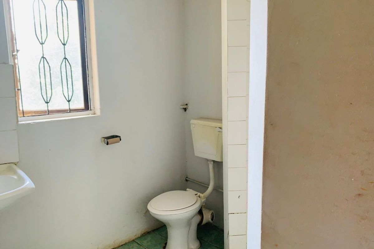 A small, dated bathroom featuring a basic toilet, wall-mounted basin, and tiled flooring, requiring cosmetic updates and modernization.