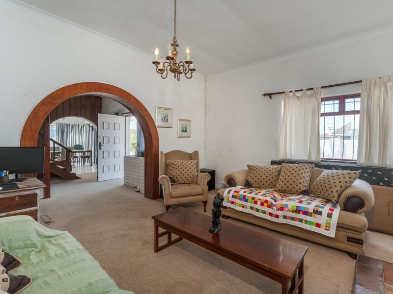 A living room featuring a distinctive arched timber doorway leading to an adjacent space, coved ceilings, and windows fitted with security bars.