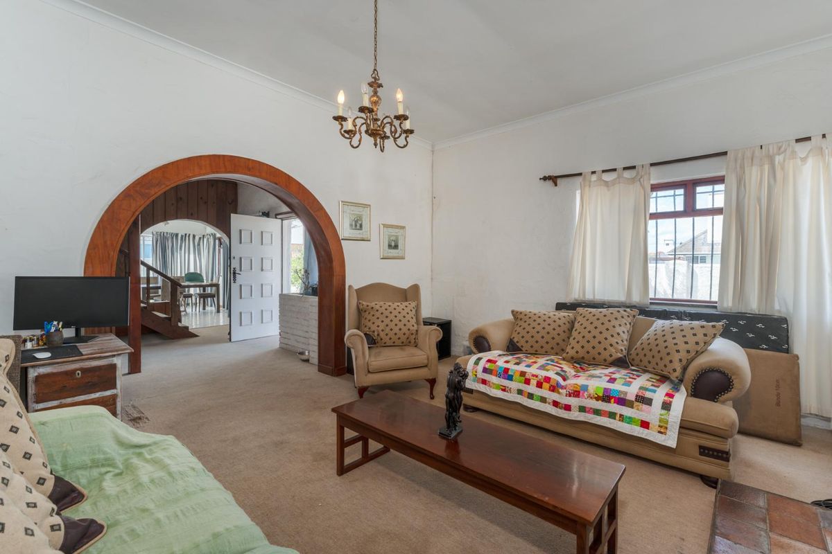 A living room featuring a distinctive arched timber doorway leading to an adjacent space, coved ceilings, and windows fitted with security bars.