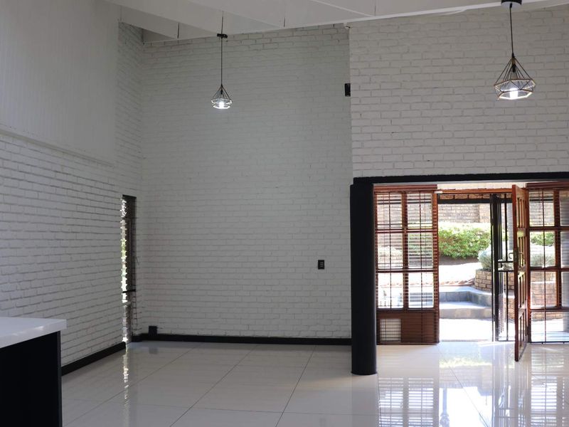 Spacious open-plan living area featuring white painted brick walls, high ceilings, polished tile flooring, and direct access to the rear garden through timber doors.