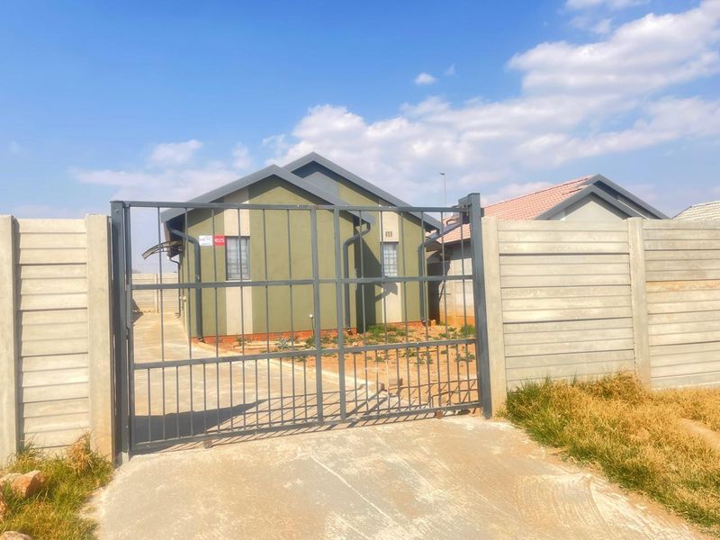 Front view of a detached house featuring a metal driveway gate, precast concrete boundary walls, and a concrete driveway.