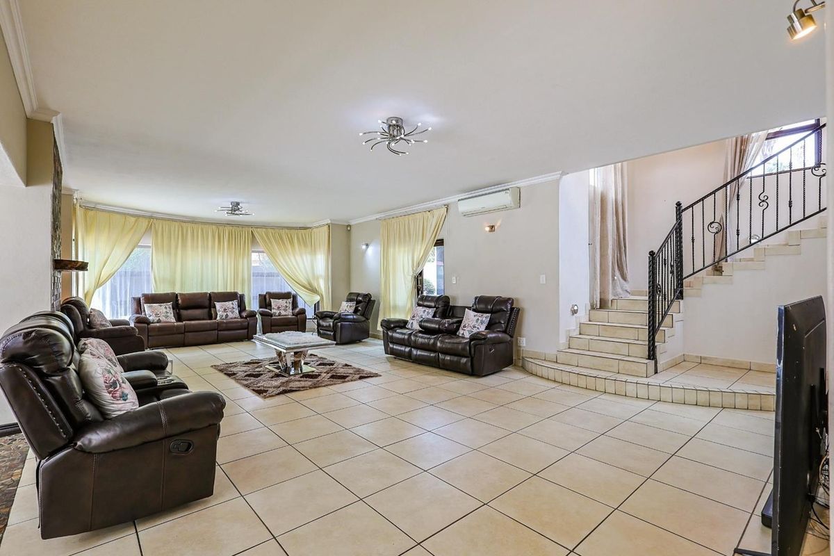 Spacious open-plan living area featuring tiled flooring, a built-in staircase with wrought iron railing, and a wall-mounted air conditioning unit.