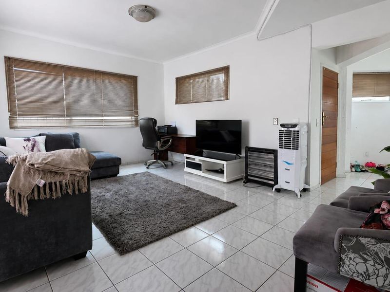 A spacious living room featuring tiled flooring, neutral walls, and venetian blinds, offering a functional and well-lit area for relaxation.