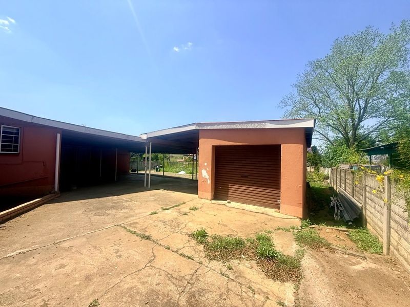 Exterior view of a detached garage with a roller shutter door, adjacent carport, and a concrete driveway area.