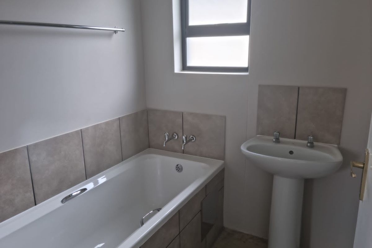 A functional bathroom featuring a built-in bathtub with tiled surround, a pedestal basin, and a window for natural light.