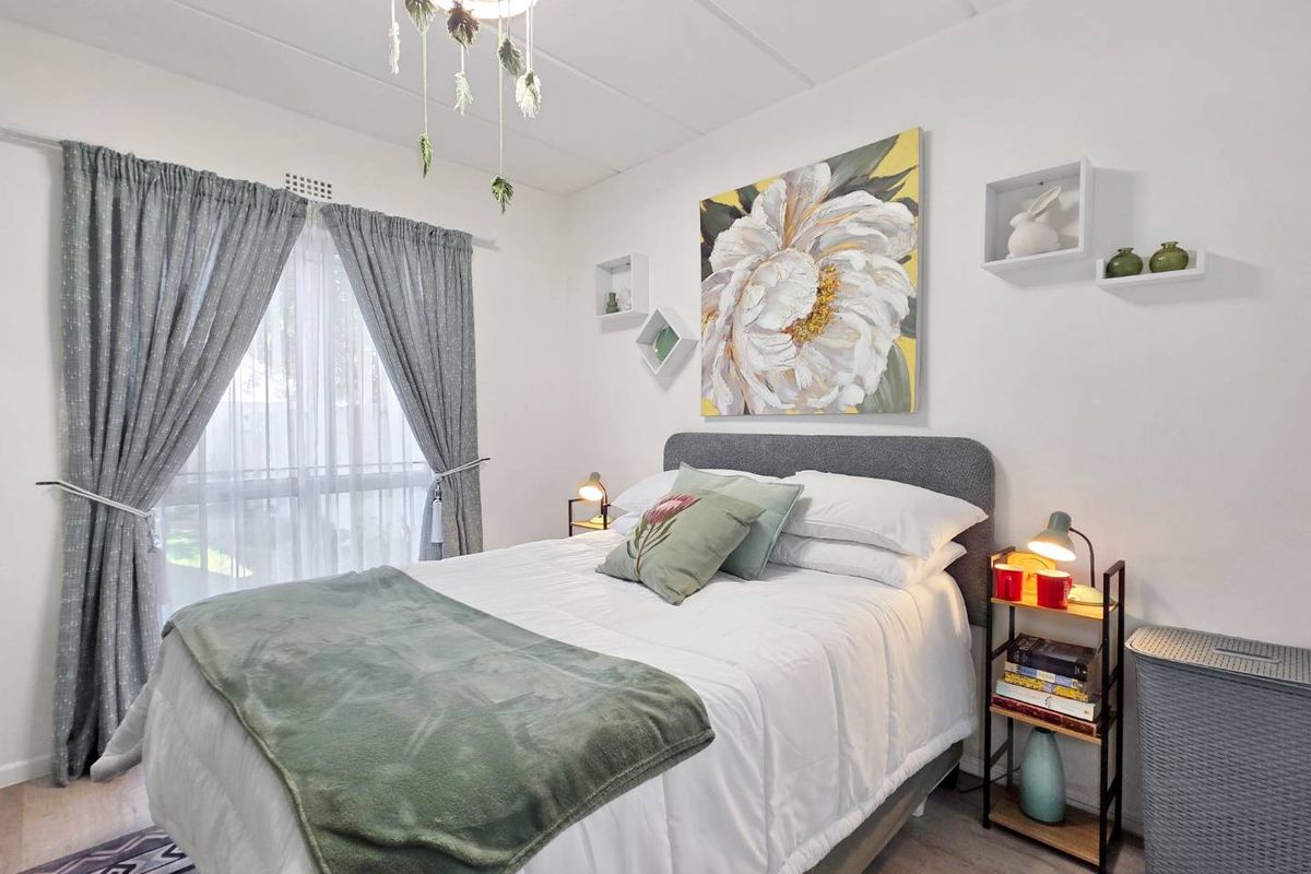 A well-maintained bedroom featuring neutral walls, laminate flooring, and a large window with curtain treatments.