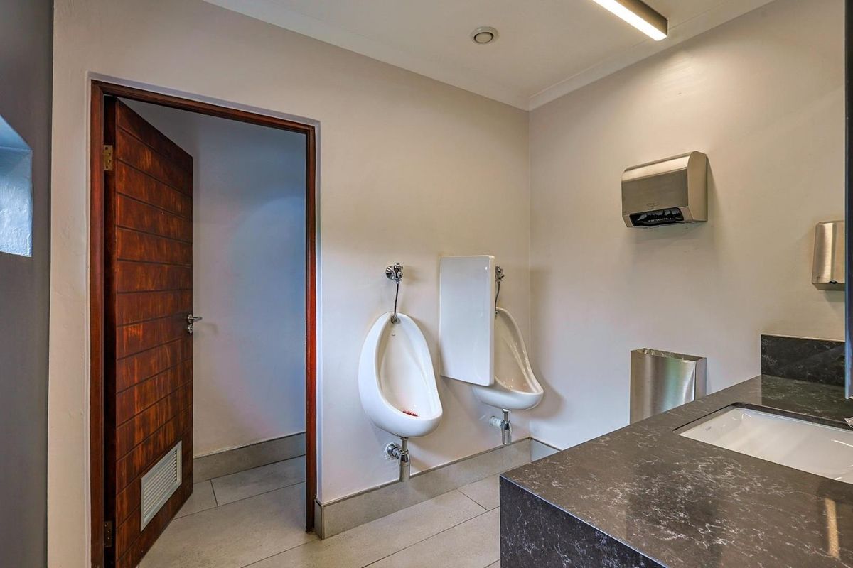 A clean, modern commercial restroom featuring wall-mounted urinals, a stone-topped vanity with integrated sink, and a wooden door.