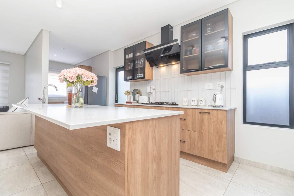 Modern kitchen featuring wood veneer cabinetry, quartz countertops, a central island, and integrated gas hob with extractor fan.