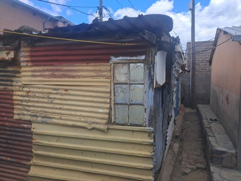 Exterior view of a structure featuring corrugated iron cladding and a metal window frame, showing significant signs of wear and structural deterioration.