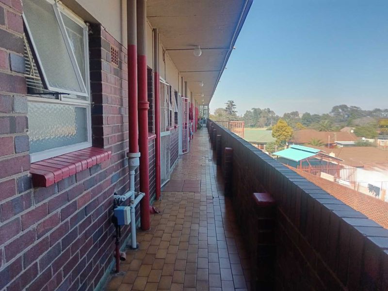 An exterior open-air apartment walkway featuring brick construction, tiled flooring, and a brick balustrade overlooking the surrounding neighborhood.