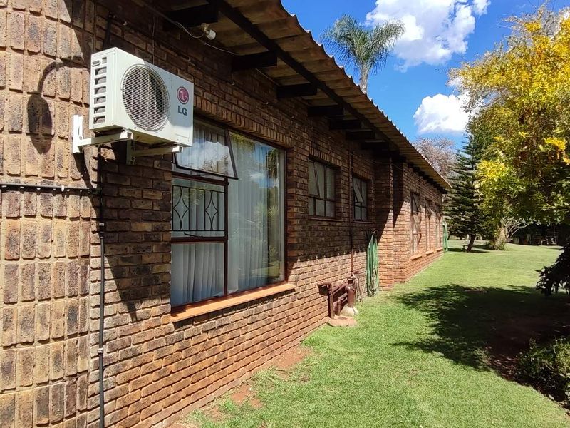 A view of the rear exterior featuring a face brick facade, established garden, and wall-mounted air conditioning unit.