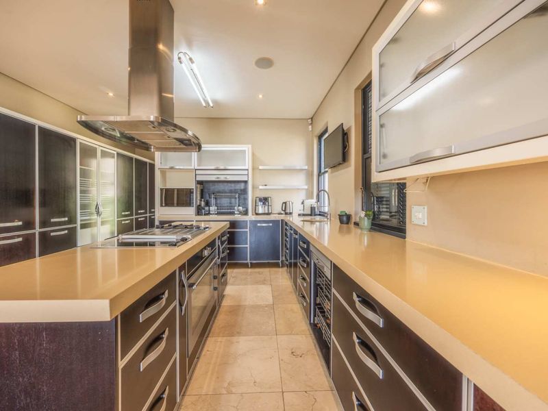 Modern kitchen featuring a central island with gas hob, stainless steel extractor, stone countertops, and extensive built-in cabinetry with integrated appliances.
