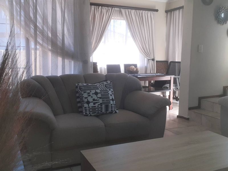 A living room area featuring tiled flooring and an adjacent staircase, with natural light filtering through window curtains.