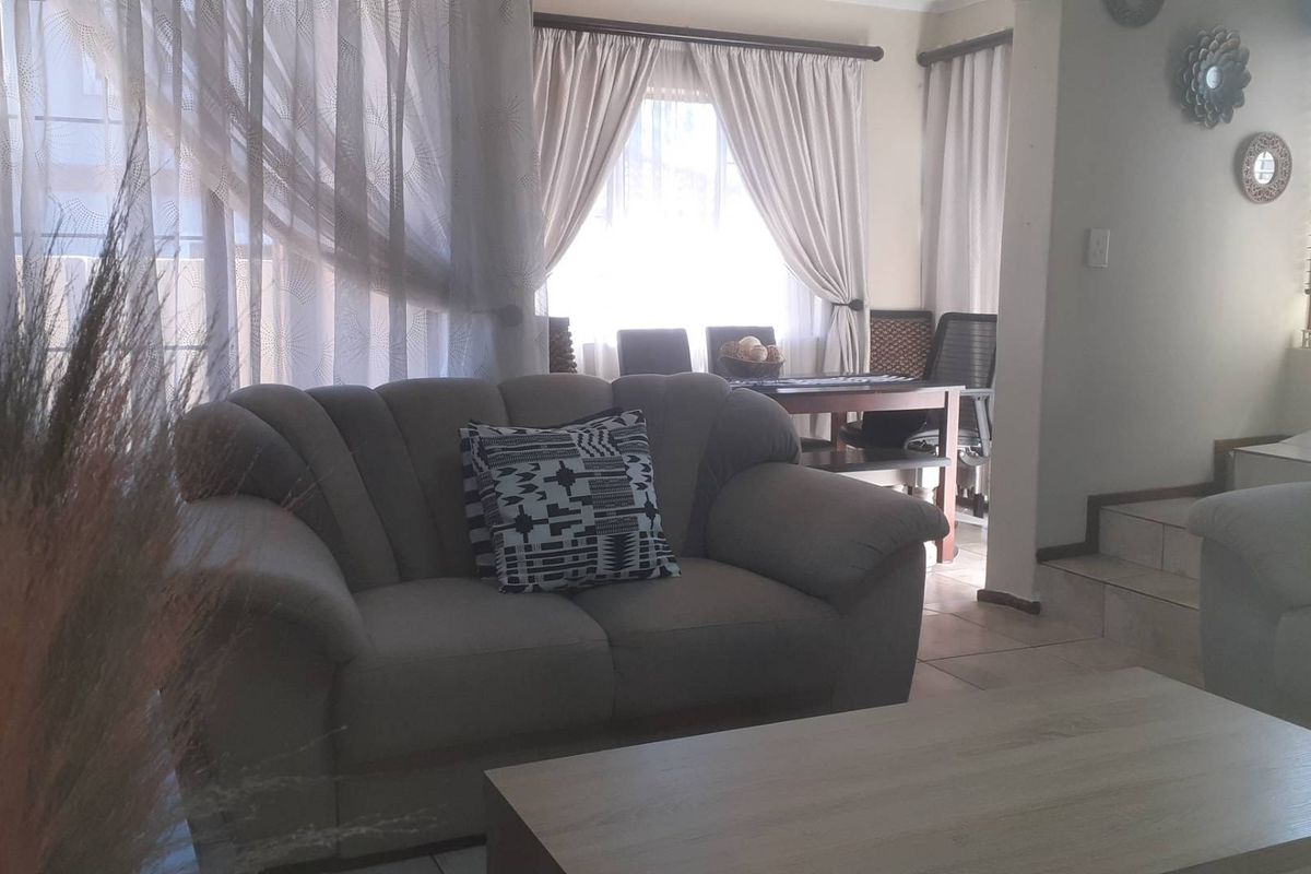 A living room area featuring tiled flooring and an adjacent staircase, with natural light filtering through window curtains.