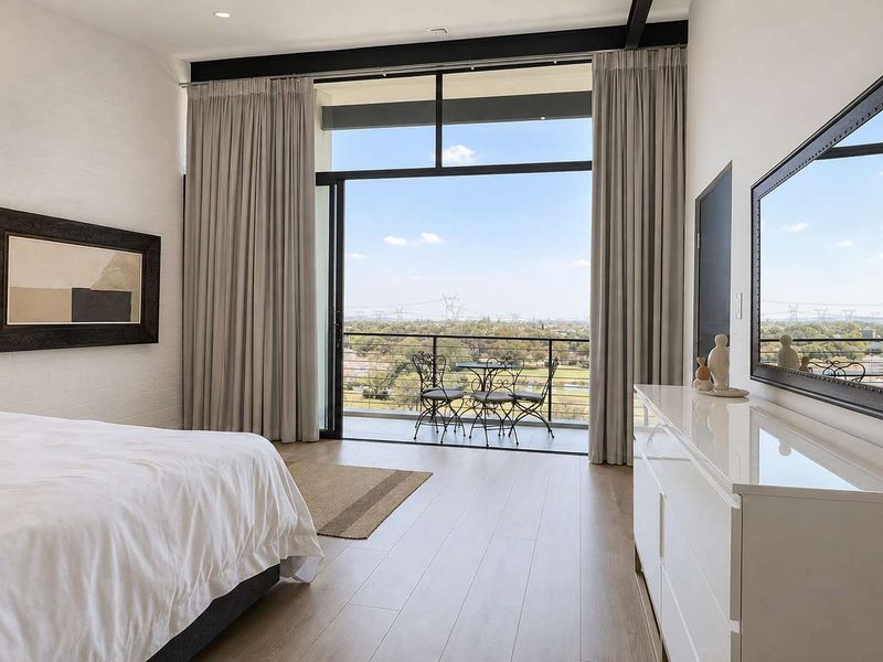 Spacious bedroom featuring floor-to-ceiling sliding glass doors that open onto a private balcony with expansive views and modern laminate flooring.