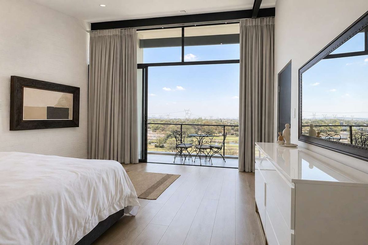 Spacious bedroom featuring floor-to-ceiling sliding glass doors that open onto a private balcony with expansive views and modern laminate flooring.