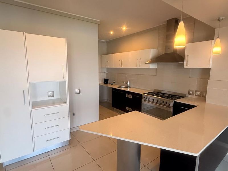 Modern kitchen featuring white and dark cabinetry, stone countertops, stainless steel appliances, and tiled flooring in an open-plan layout.