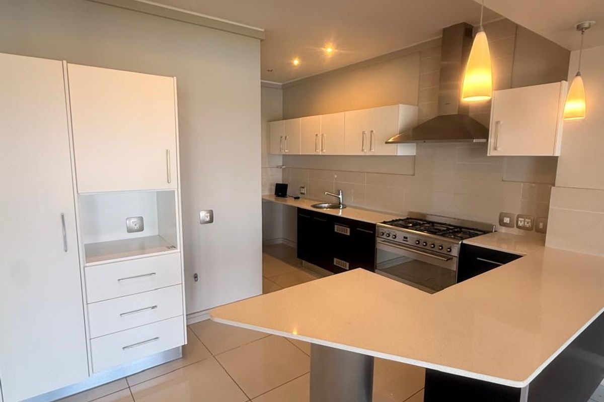 Modern kitchen featuring white and dark cabinetry, stone countertops, stainless steel appliances, and tiled flooring in an open-plan layout.