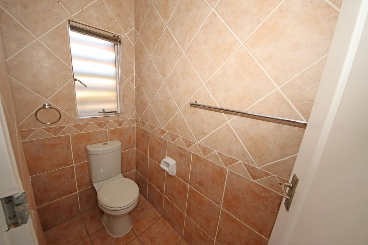A compact guest toilet featuring floor-to-ceiling ceramic tiling, a standard toilet suite, and a small louvered window for ventilation.