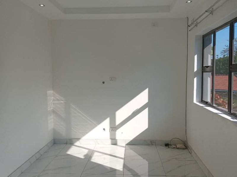 A bright, empty living room featuring modern marble-look floor tiles, a tray ceiling with recessed lighting, and large windows allowing for ample natural light.