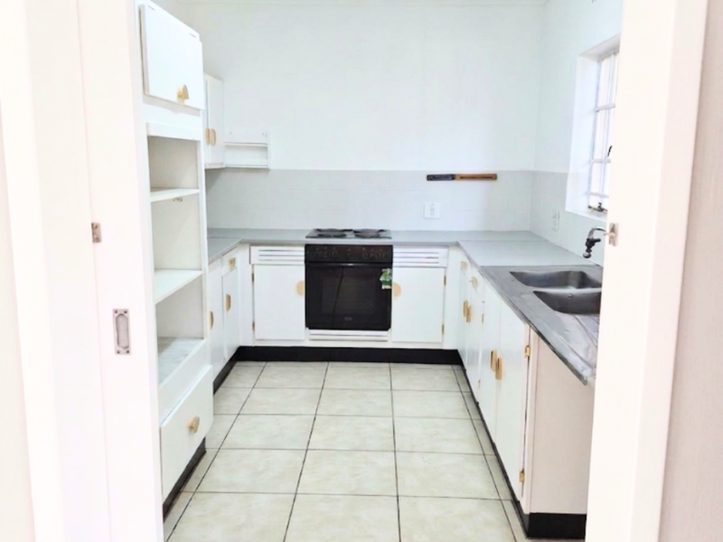 A functional, empty kitchen featuring white built-in cabinetry, a built-in oven with hob, double sink, and tiled flooring.