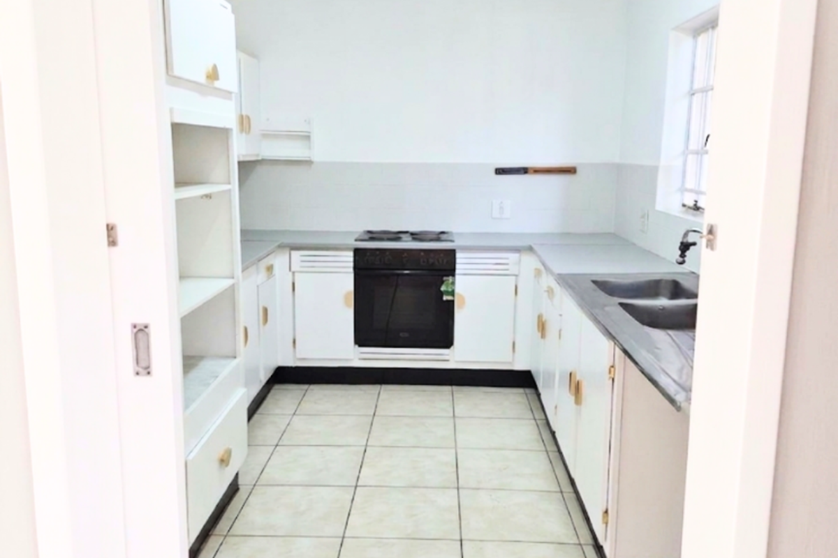 A functional, empty kitchen featuring white built-in cabinetry, a built-in oven with hob, double sink, and tiled flooring.