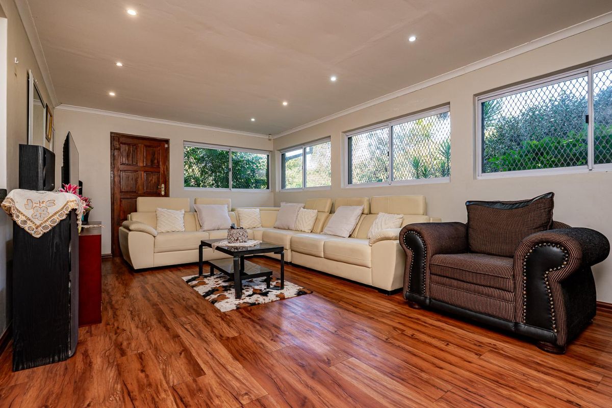 Spacious living room featuring warm-toned laminate flooring, recessed downlighting, and multiple windows fitted with security mesh screens.