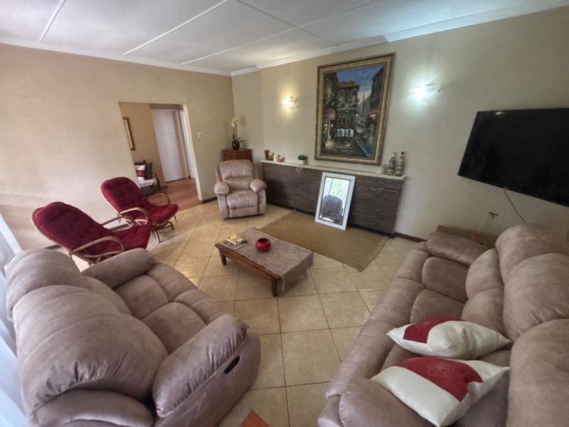 A spacious living room featuring neutral tiled flooring, wall-mounted lighting, and a built-in low-level display shelf.