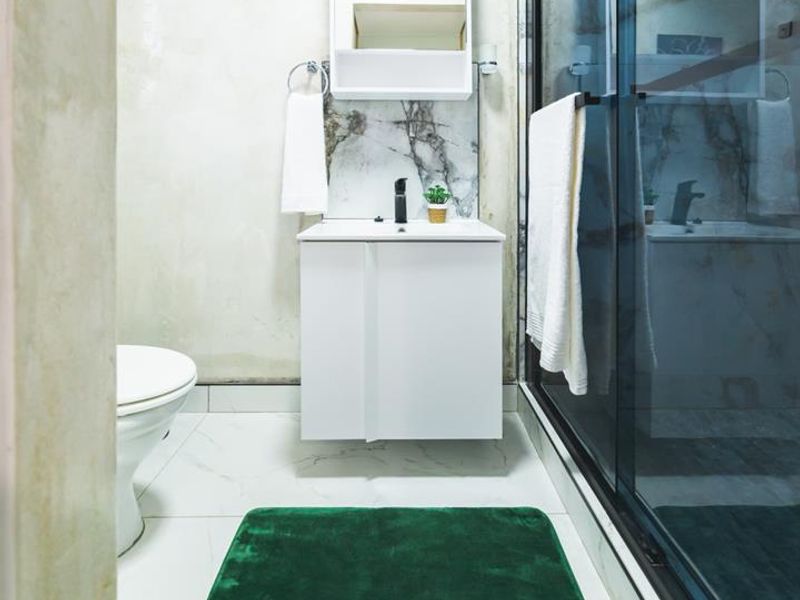 A compact bathroom featuring a modern vanity, shower enclosure, and toilet, with unfinished wall surfaces requiring final plastering or painting.