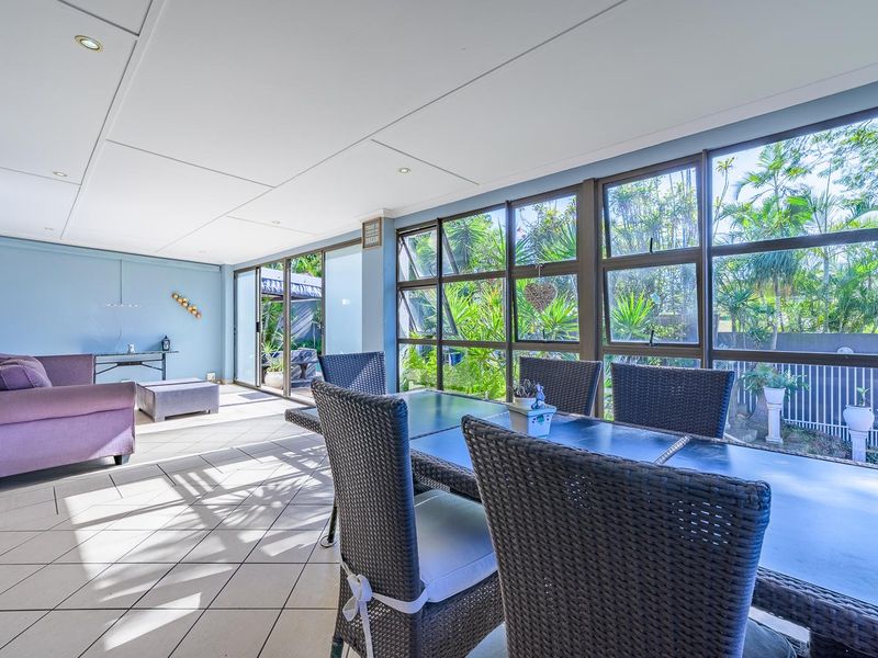 A bright, enclosed patio area featuring tiled flooring, recessed lighting, and large windows providing views of the garden.