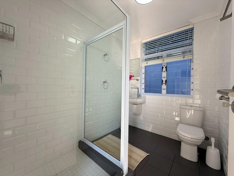 A modern, well-maintained bathroom featuring a glass shower enclosure, wall-mounted basin, toilet, and clean white subway tile finishes.
