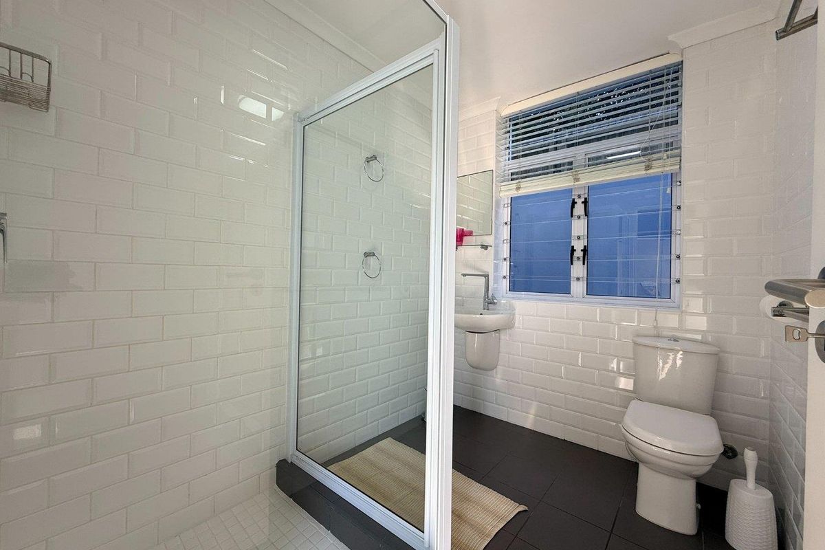 A modern, well-maintained bathroom featuring a glass shower enclosure, wall-mounted basin, toilet, and clean white subway tile finishes.