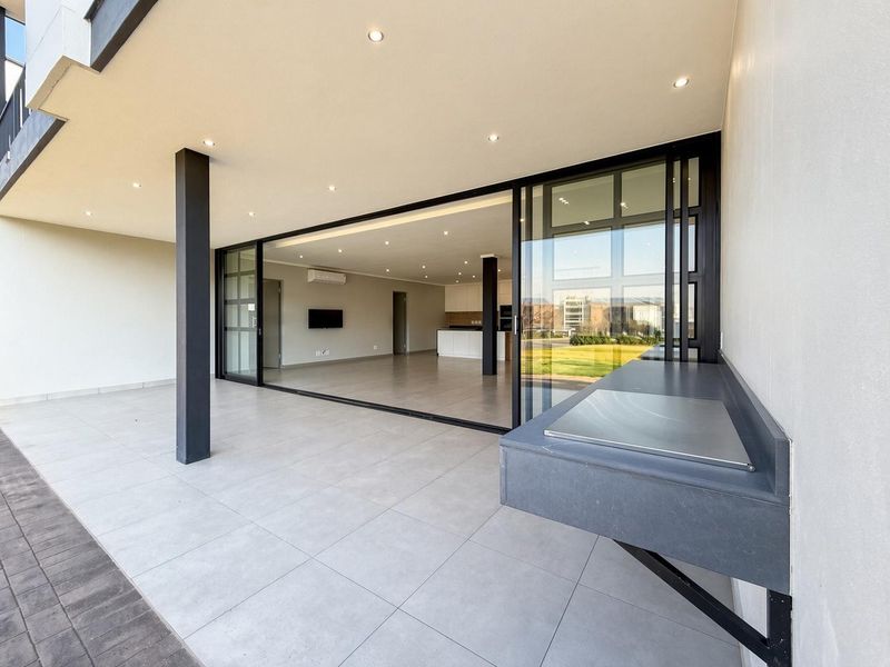 Spacious covered patio featuring a built-in braai, modern tiled flooring, and large sliding glass doors providing seamless access to the open-plan interior living area.