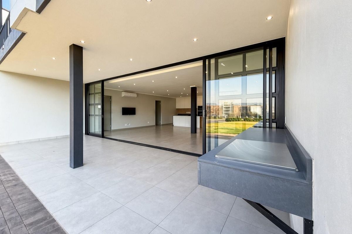 Spacious covered patio featuring a built-in braai, modern tiled flooring, and large sliding glass doors providing seamless access to the open-plan interior living area.