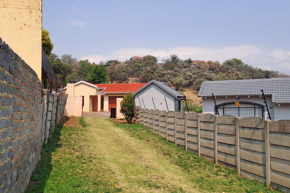 Rear view of the property showing a driveway, precast concrete boundary walls with electric fencing, and multiple residential structures with tiled roofs.