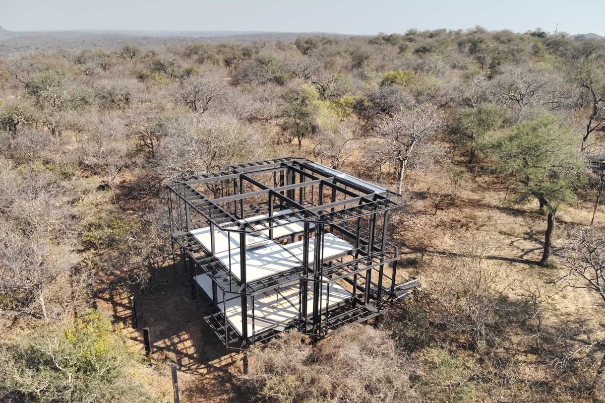 Aerial view of a property under construction, featuring a steel structural frame and concrete floor slabs set within a natural bushveld environment.